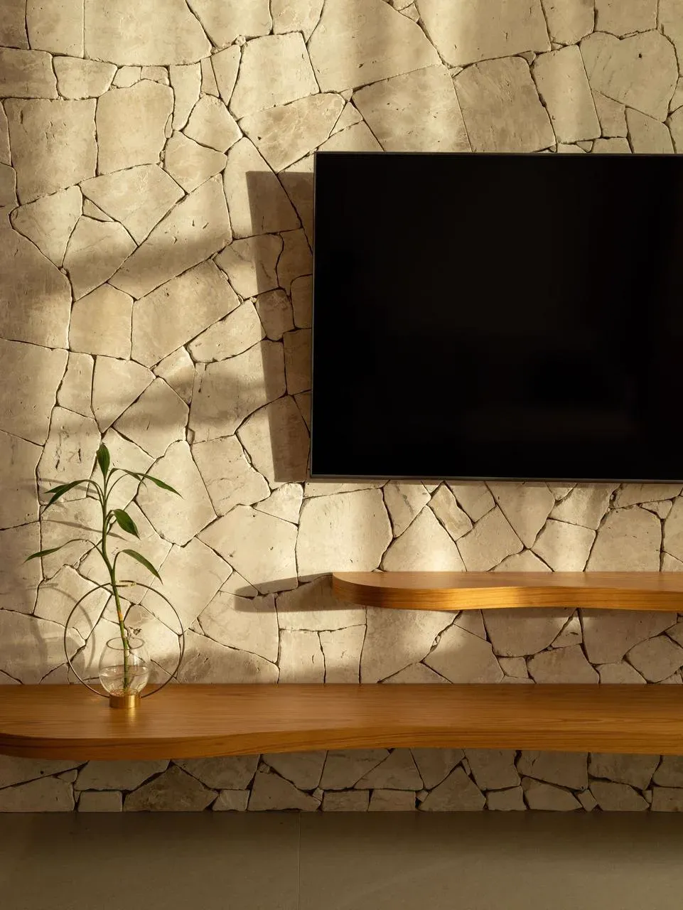 Painel de televisão sobre parede de pedra natural com prateleira curva em madeira